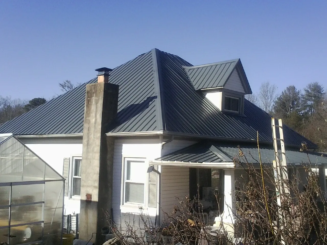 Dark blue standing seam metal roof on a white farmhouse with dormer — Slate & Tile Roof Repair by Roofing Brothers in Bankston