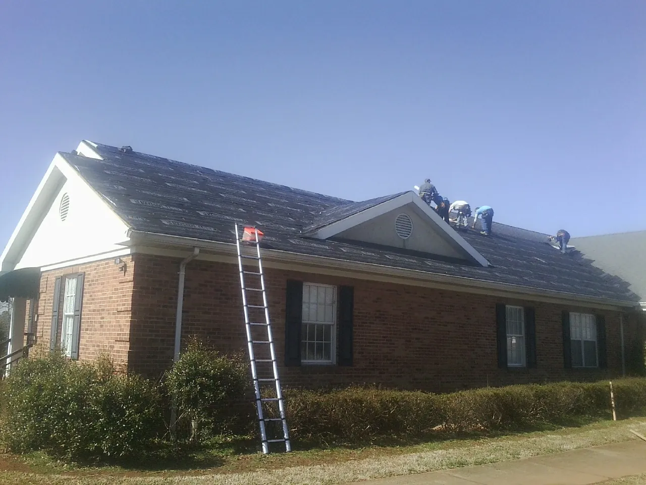 Crew tearing shingles off a brick ranch roof with a ladder set — Emergency Roof Repair work by our crew in Bankston