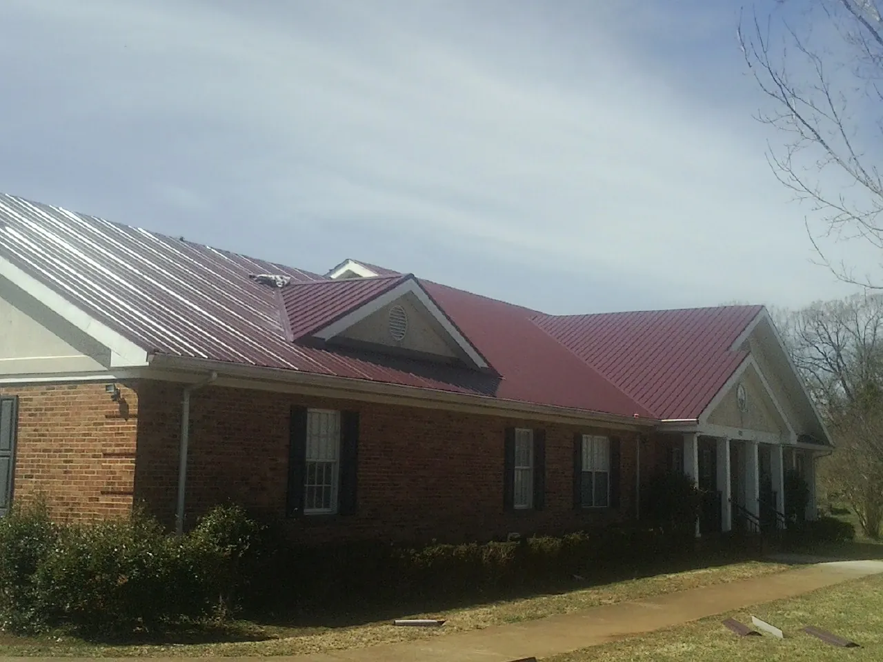 Red metal roof with gabled entries on a long brick building, from a Hail Damage Roof Repair job in Bankston