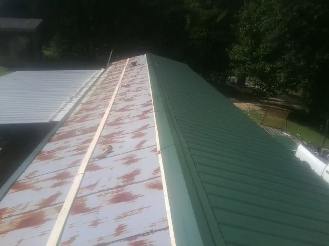 Old rusted panels beside newly installed green metal roofing — Wind Damage Roof Repair by Roofing Brothers in Bankston