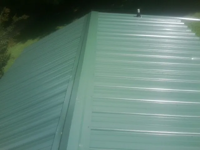 New green metal panels meeting at the ridge of a roof — Flat Roof Repair work by our crew in Bankston