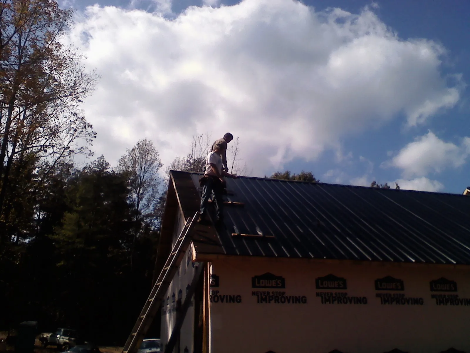 Roofer fastening dark metal panels high against a cloudy sky, from a Roof Inspection job in Bankston