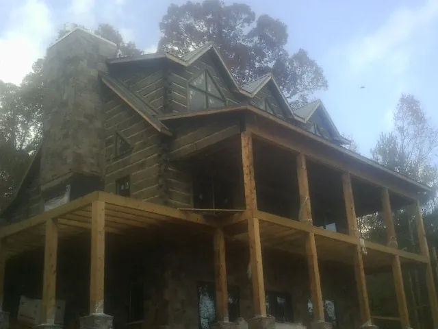 Stone chimney and dormers on a large log home with a timber porch in Bankston