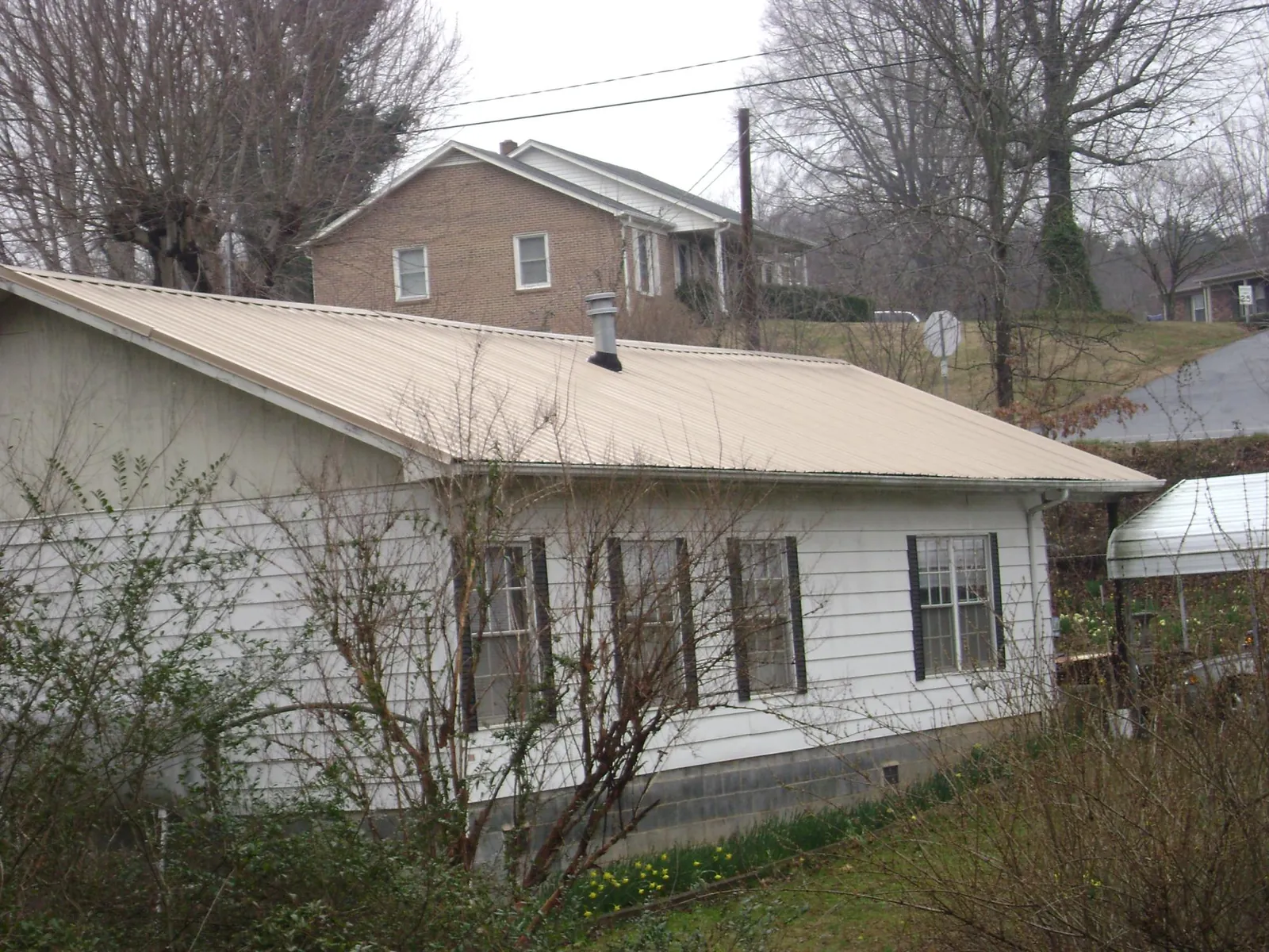 Tan metal roof on a white sided house set into a hillside — Commercial Roofing by Roofing Brothers in Bankston