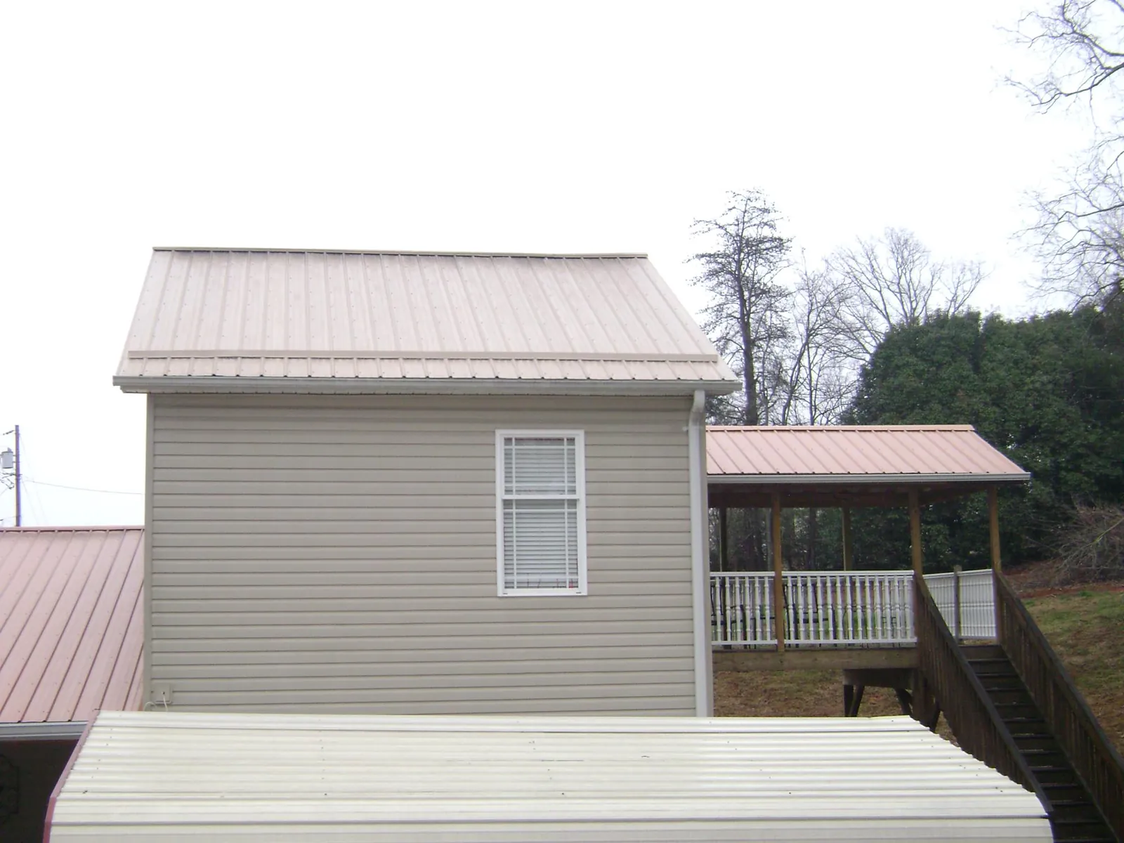 Tan metal roofs on a two story addition and attached porch, from a Roof Replacement job in Bankston